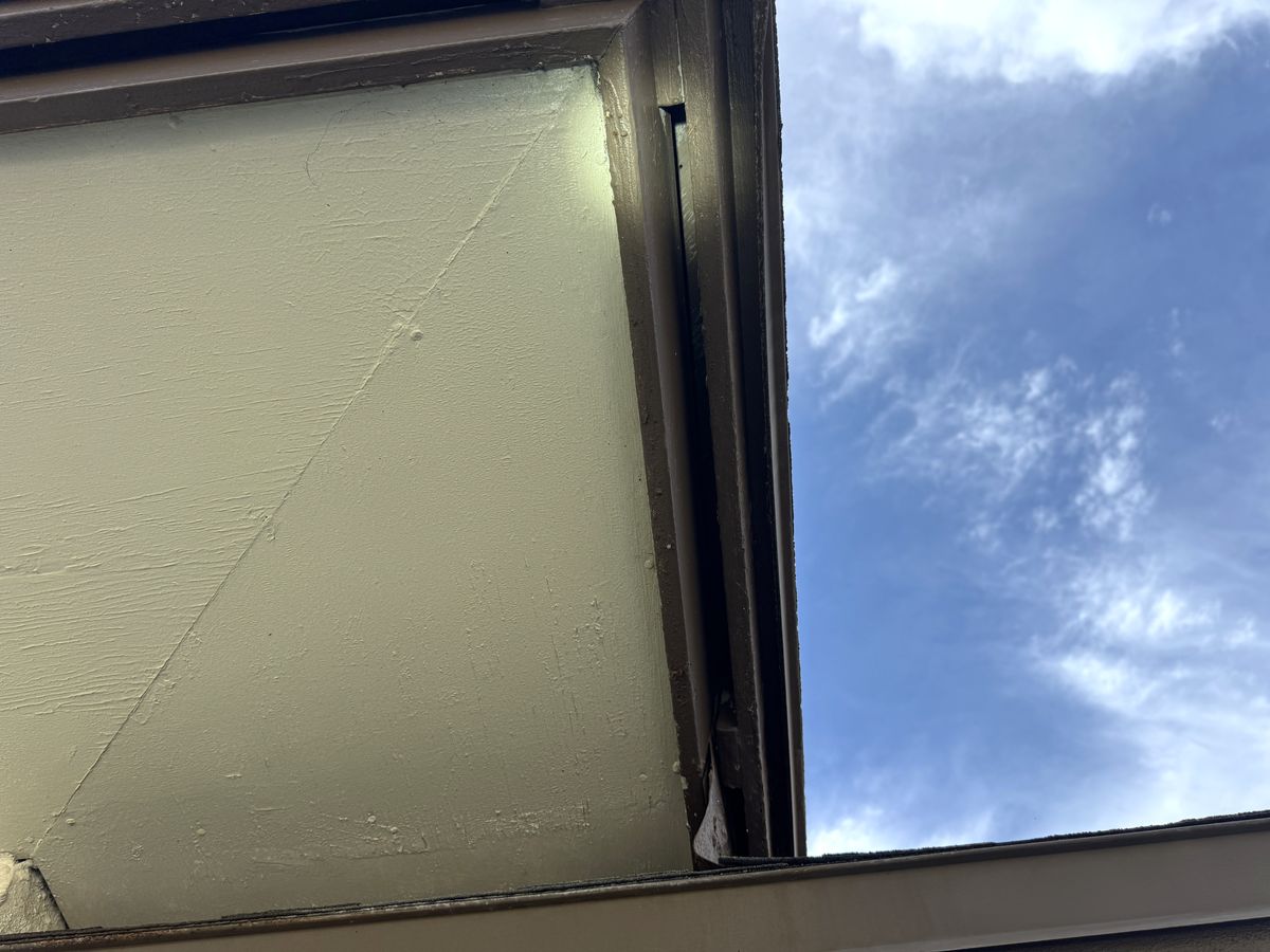 Looking up at an eave corner: a dark open slot runs down the fascia where it meets the soffit.